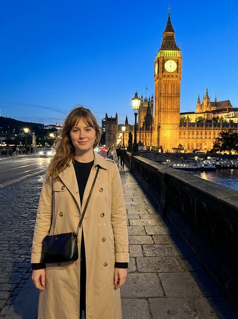 Reference: a woman in a trench coat on a bridge, clock tower behind her